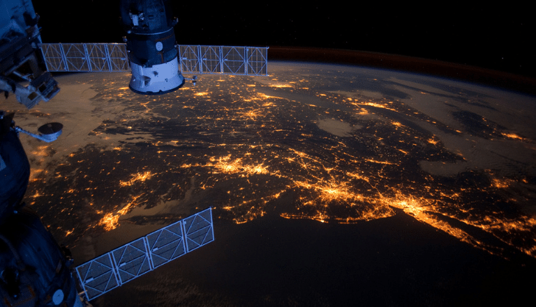 Section of the International Space Station pictured above Earth in darkness, with the lights of the cities lit up